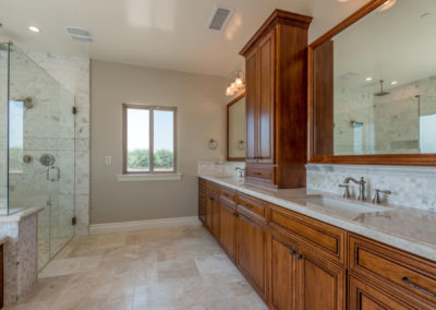 Long bathroom with glass shower and two sinks with built in cabinets