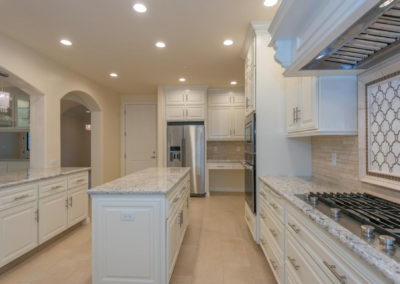 White kitchen with island, stove top and arched doorway