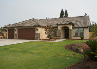 Tan home with stone accents and grass with grey sky