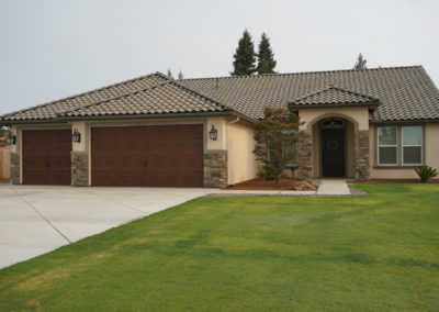 Tan home with stone accents and grass with grey sky
