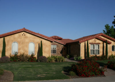Tan home with clay shingles, grass and flowers
